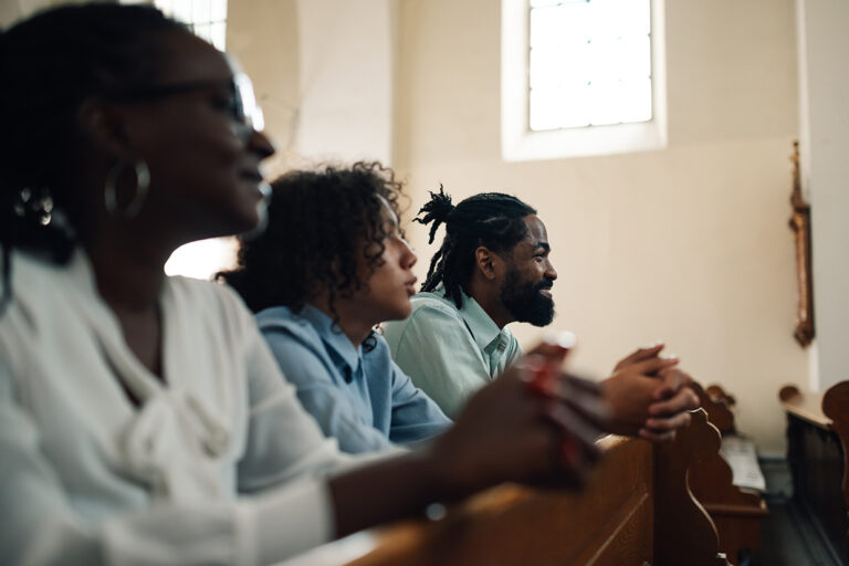 Family praying together in church pew holding hands